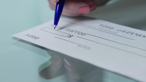 business woman hand signs and filling bank check for one thousand 1000 dollars