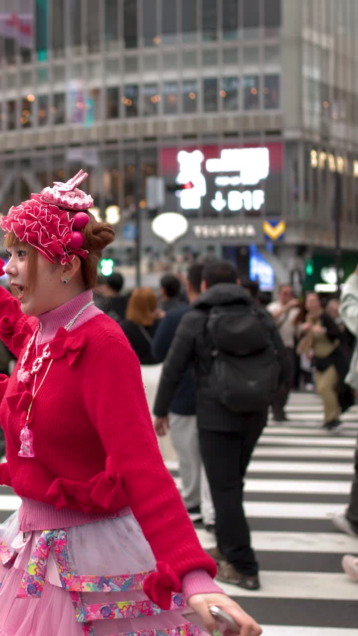A woman wearing vibrant pink decora fashion dances and laughs at a busy pedestrian crossing