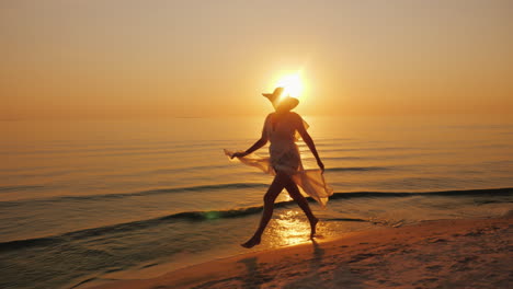 una mujer con un vestido ligero camina descuidadamente por la orilla del mar al atardecer
