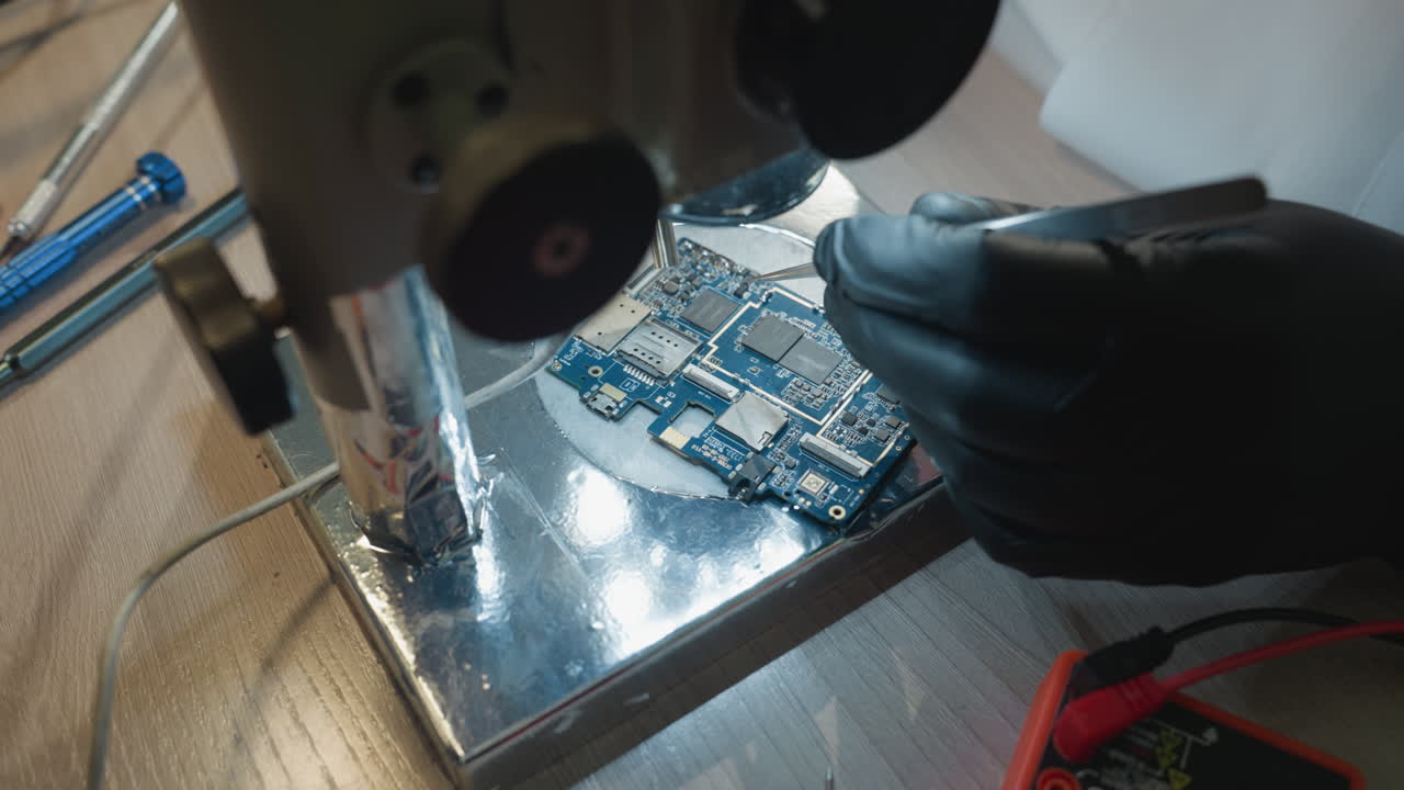 Close-up view of a technician working on a circuit board on a lab workbench, various precision tools, including tweezers and screwdrivers, are scattered around