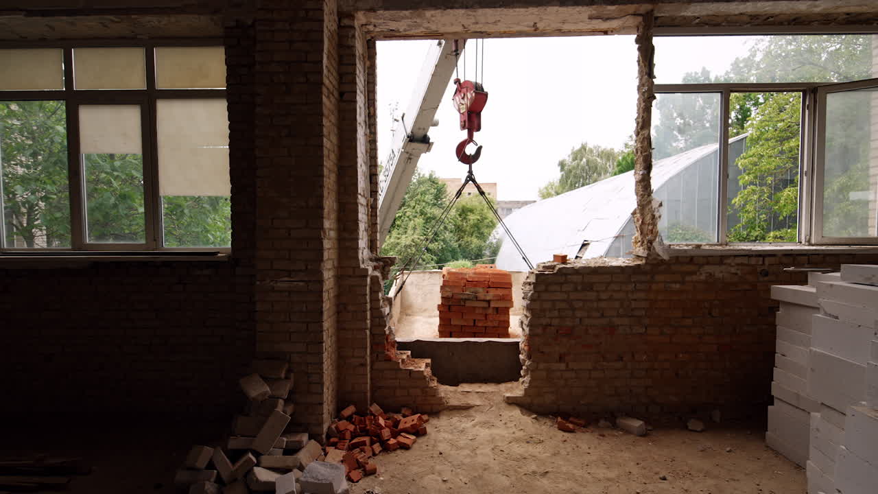 A pile of orange bricks hanging on the hook of an excavator outside the building. Entering the room under construction.
