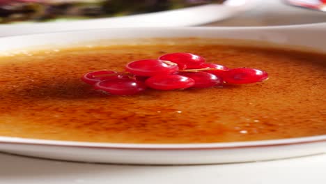 close-up of a creamy crème brûlée dessert topped with red currants