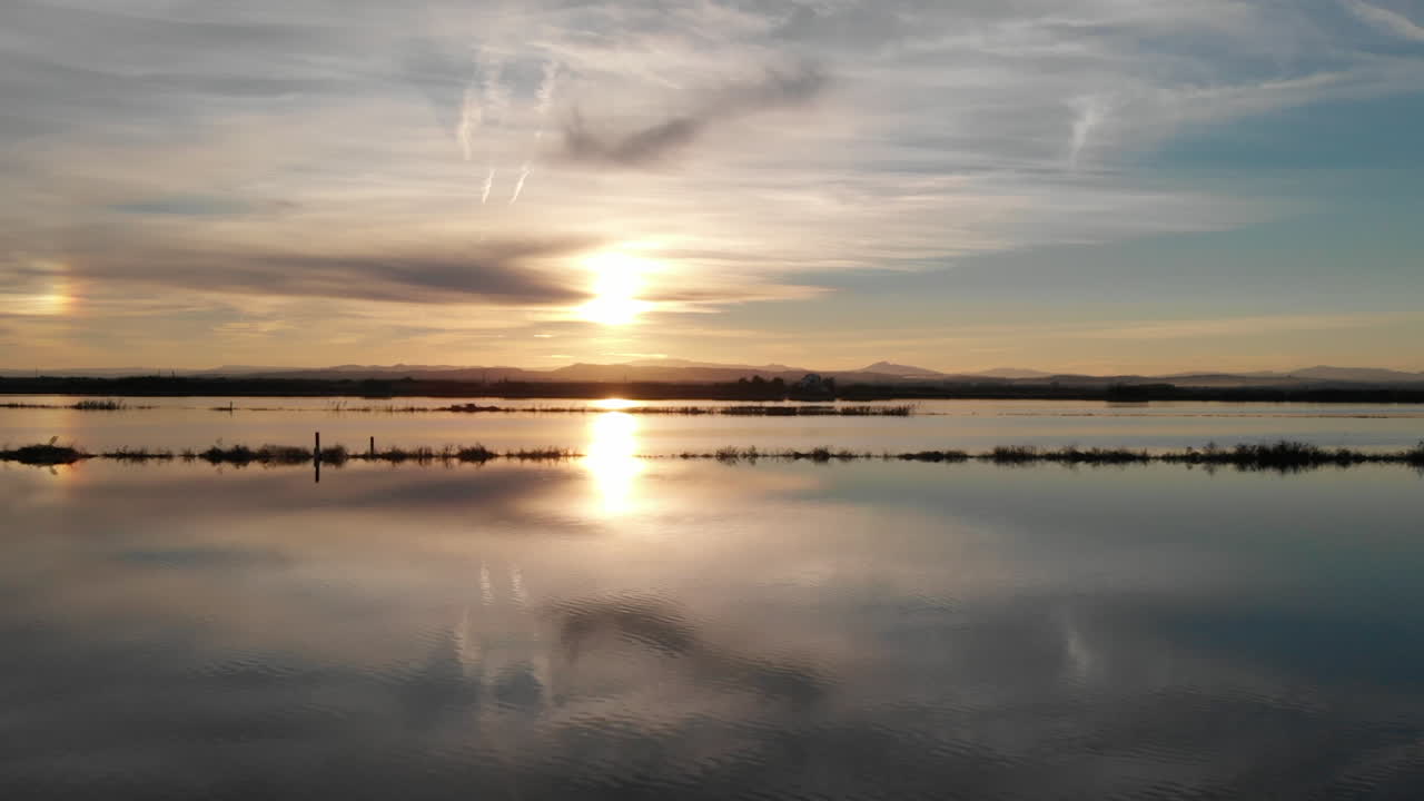 Aerial view flying from right to left. Beautiful sunset over the rice field covered with water. Perfectly smooth surface of water in Albufera National park, Valencia Spain