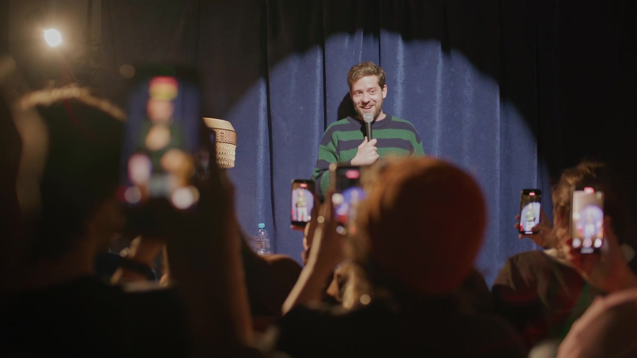 Comico uomo che si esibisce sul palco mentre gli spettatori lo riprendono con i telefoni