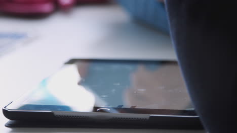 boy’s hands using stylus and tablet computer in primary school classroom, close up, selective focus