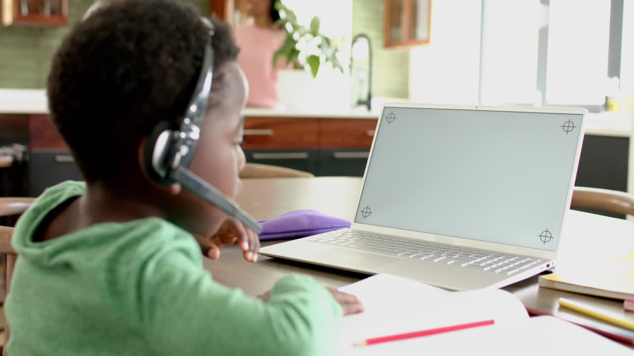 African american boy having online class using headphones and laptop with copy space, slow motion