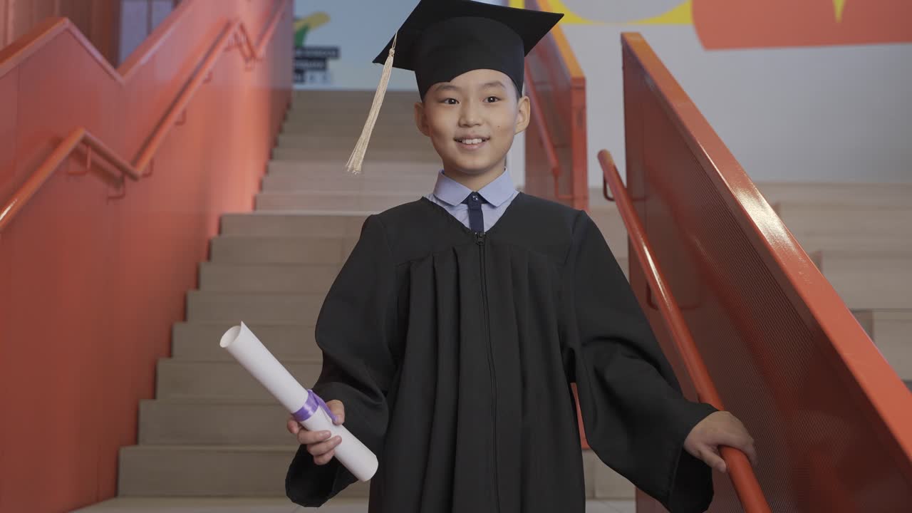 모자와 가운을 입고 졸업 졸업장을 들고 카메라를 바라보는 행복한 아시아 유치원 남학생의 초상화