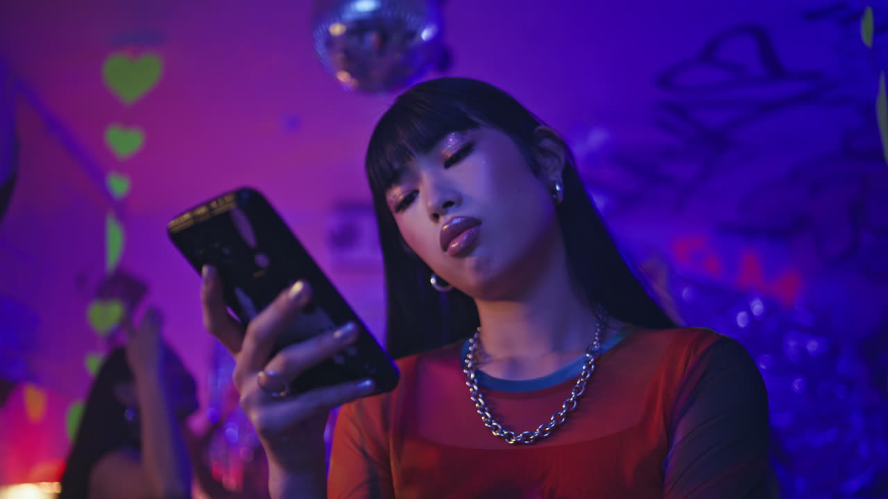 Clubbing woman browsing cellphone in neon nightclub lights closeup. Club style