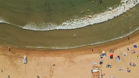 Drohnenaufnahme-Von-Oben-Nach-Unten,-Die-Einen-Belebten-Strand-Voller-Begeisterter-Schwimmer-Und-Sonnenbadender-Familien-Einfängt-Und-Unvergessliche-Erinnerungen-An-Die-Sommerferien-Schafft