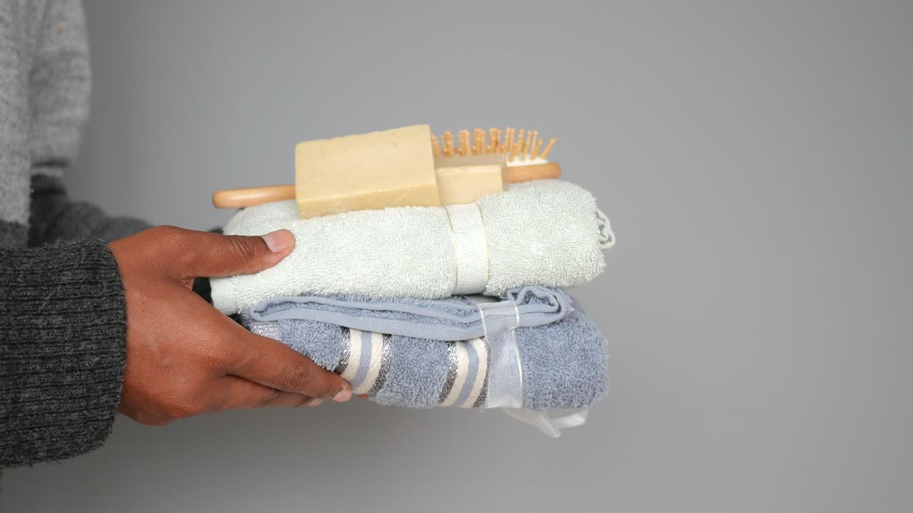 Hands holding a stack of clean towels, soap, and brushes for personal care