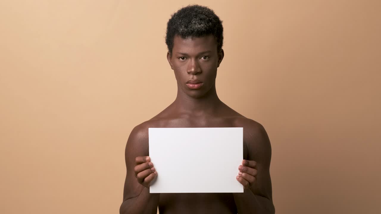 Serious african young man shirtless holding a blank panel over beige background