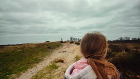 Blond-girl-with-ponytale-walking-on-dune-hill-with-sand-on-cloudy-windy-day