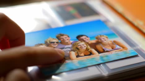 a hand selecting a cherished photograph from a collection, featuring friends enjoying a joyful day at the beach in a vibrant blue background