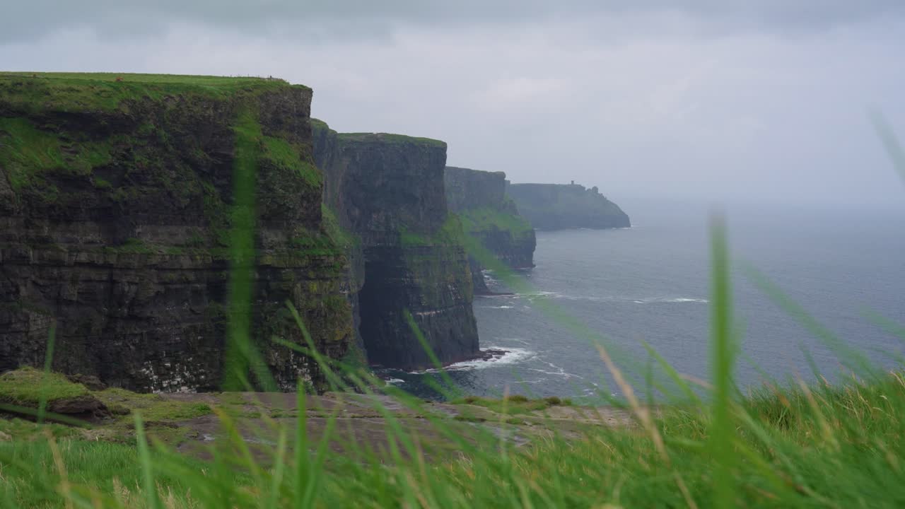 A moody and atmospheric wide shot of the famous Cliffs of Moher in Ireland. The dramatic sea cliffs stretch into the distant mist under an overcast sky