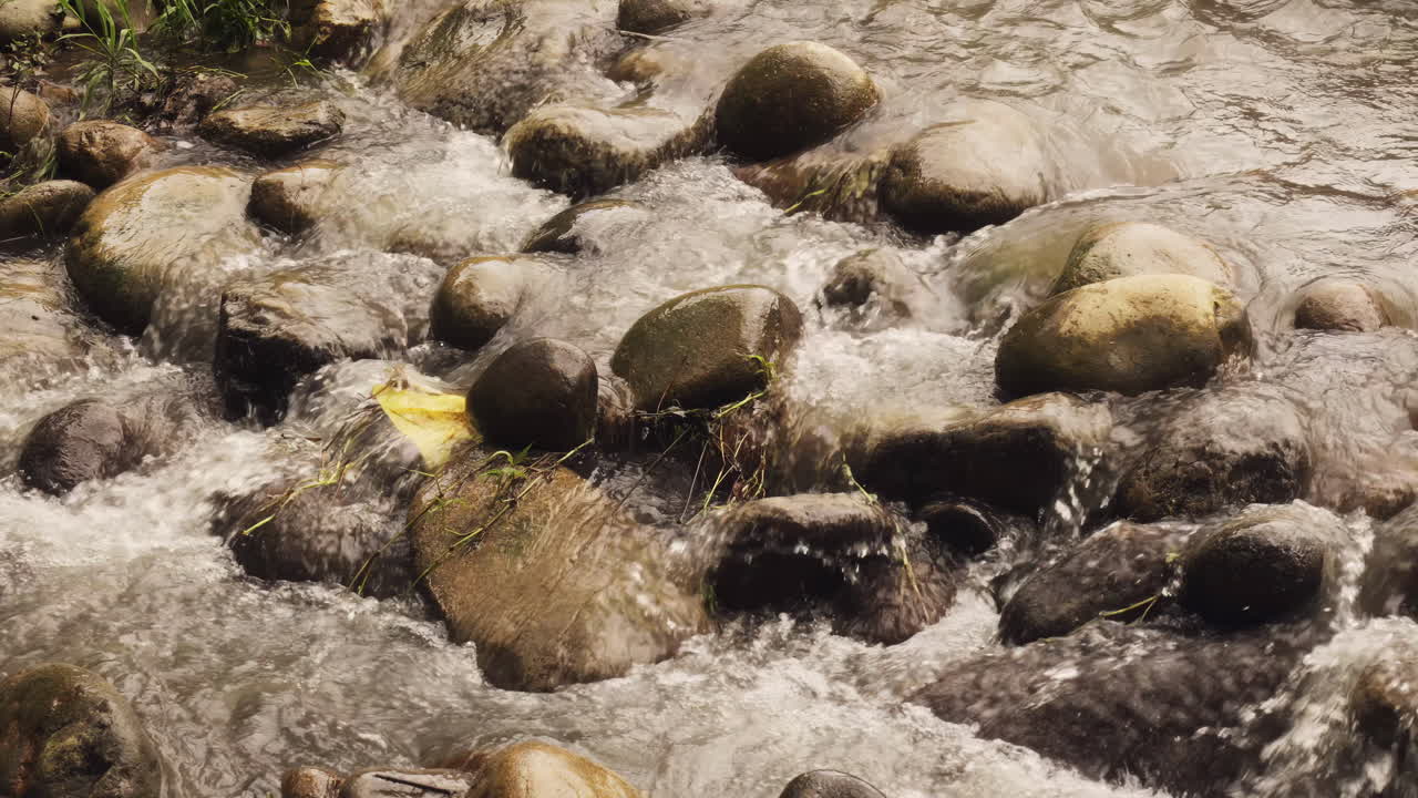 Serene river stream cascades over smooth rocks in a lush, natural setting. Crystal-clear water flows gently, reflecting sunlight