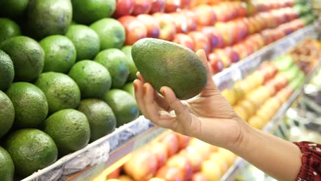 persona con un aguacate en una tienda de comestibles