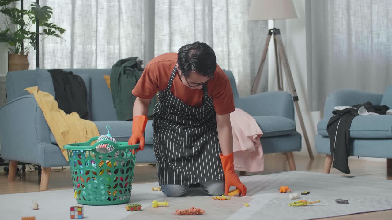 Asian Male Housekeeper With An Apron Cleaning The Messy Room From Toys