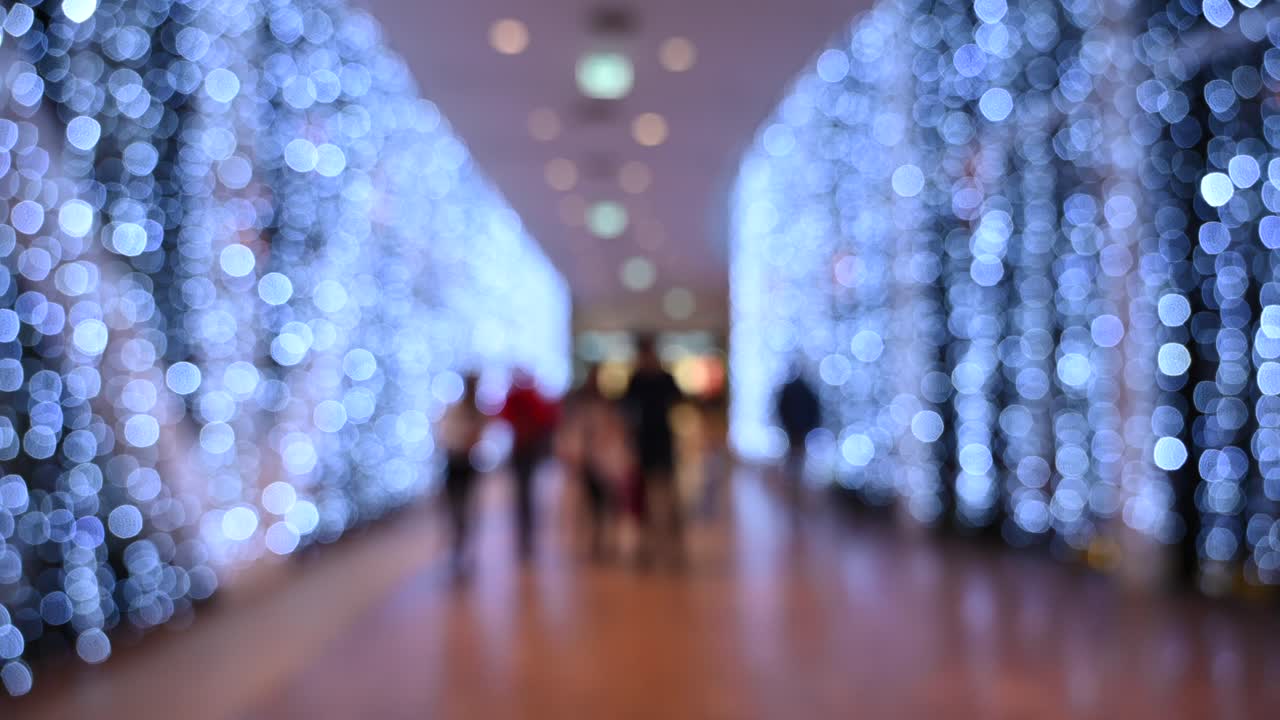 Blurred view of people walking through a shopping mall with Christmas lights on the walls