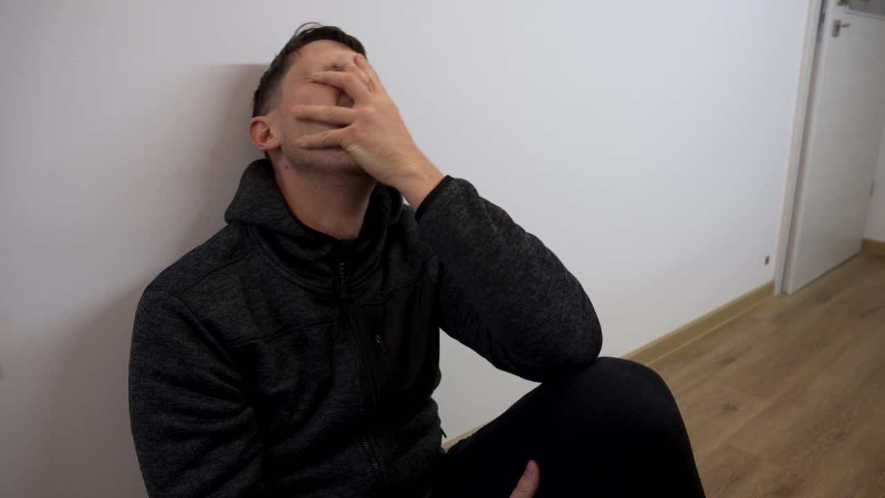 Young emotional man sitting in room on floor with profound sadness and anguish