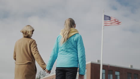 Mom-and-child-hold-hands-and-look-at-the-American-flag-in-front-of-the-office-building