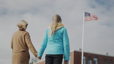 mom and child hold hands and look at the american flag in front of the office building