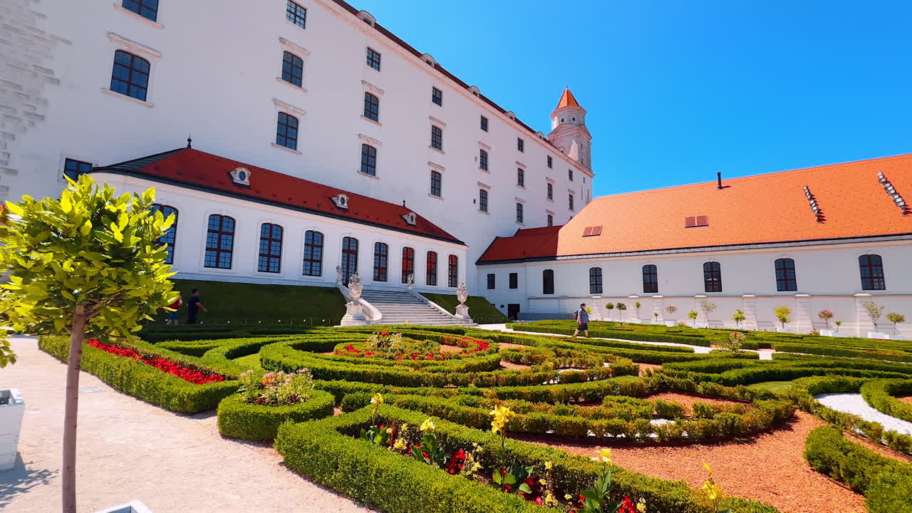 Few people walk among the beautiful flower-beds with lovely plants. Territory of the Bratislava Castle from low angle perspective