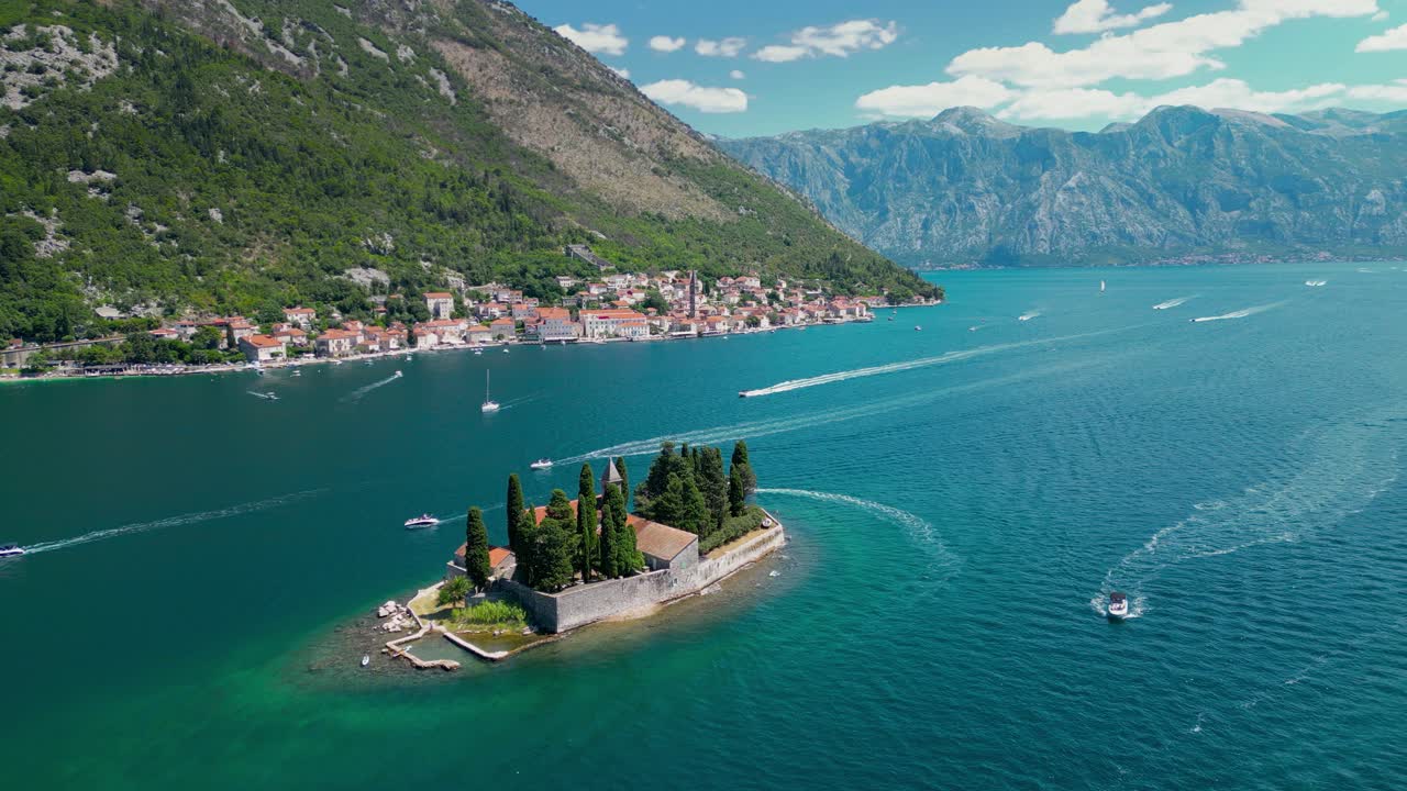 Aerial drone view of Sveti Dorde Island - Saint George Monastry in the middle of the island. Static footage. In background is Perast city. Famous travel destination in Montenegro. Boats passing.