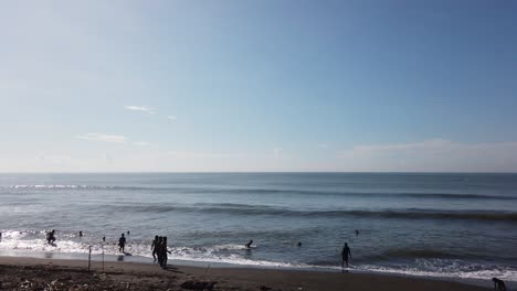 Menschen-Schwimmen-Und-Baden-Im-Schwarzen-Sandstrand-Meer,-Bali,-Indonesien-Ketewel-60-Fps-Klares-Blaues-Offenes-Himmelpanorama