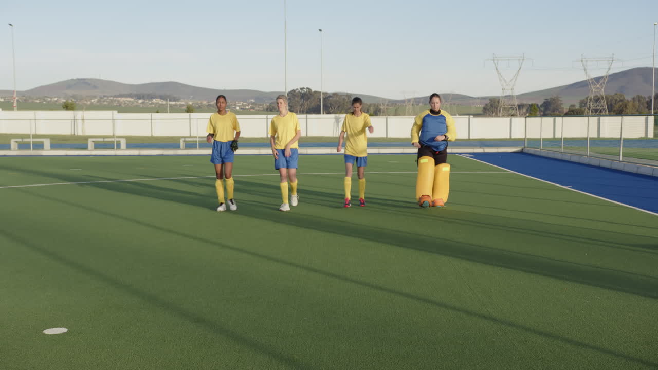 Female hockey players practicing drills on field in sunny outdoor setting