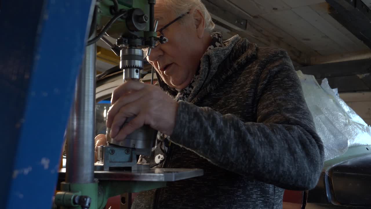 trabajador sénior limpiando y preparando la máquina de perforación en un pequeño taller oscuro