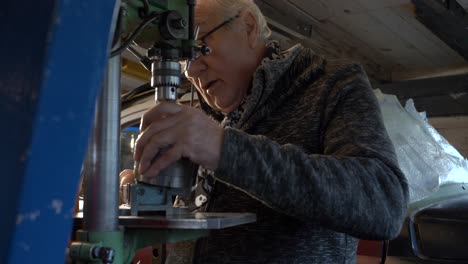 senior worker cleaning and preparing drilling machine in a small dark workshop