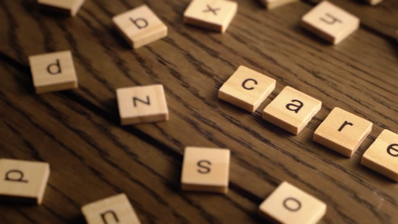 Wooden letter tiles spell the word care as the camera pans across a rustic wood surface with warm, soft lighting.