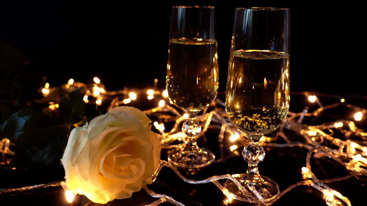 Bicchieri con champagne e rose sullo sfondo di ghirlande luminose.