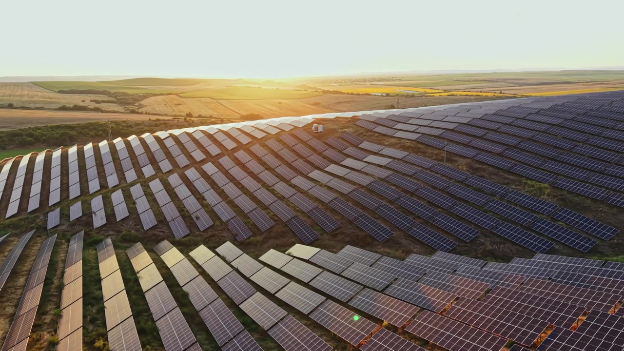 Solnedgangudsigt over en solcellepark med rækker af solpaneler designet til at udnytte solenergi, beliggende i et landområde