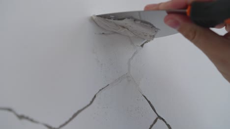 worker's hand uses putty knife in filling cracks on the wall with concrete caulk