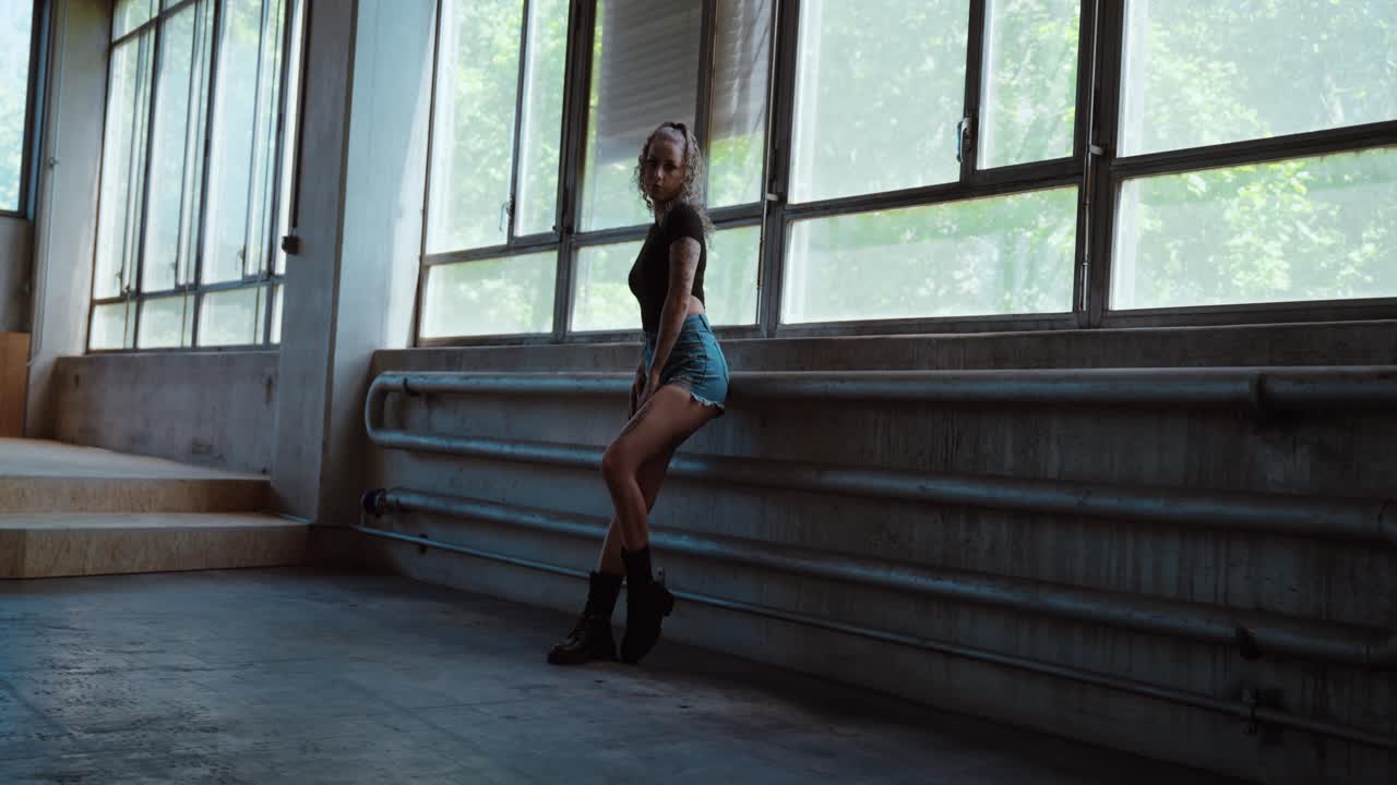 Tankefuld tatoveret kvinde, der kigger ind i kameraet og poserer i naturligt lys, iført hotpants.
