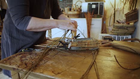 medium shot of a basketmaker shaping and weaving together wooden rods while making a traditional welsh basket by hand