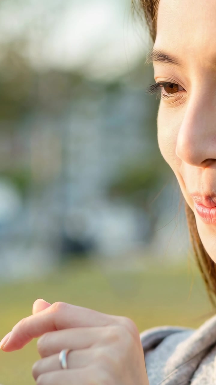 Video verticale: Donna asiatica adulta sorridente che usa il telefono al parco, indossa una felpa grigia con cappuccio e un anello