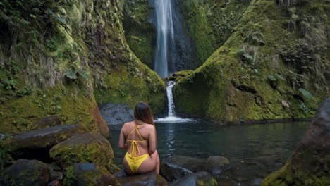 a woman stands in awe before the majestic vuelta al cañón waterfall in costa rica, surrounded by lush jungle and mist rising from the cascading water