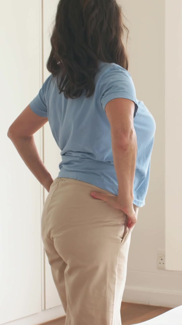 Vídeo vertical: Chegando à cama em casa, mulher de camiseta azul se levantando, olhando pela janela com uma impressora.