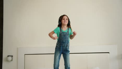 Adorable-happy-girl-jump-and-dance-with-headphones-on-bed-in-the-morning