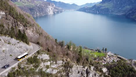 a typical yellow swiss post bus drives on a mountain road in front of the picturesque urnersee