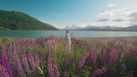 Woman-holding-lupin-flower-standing-in-dreamy-flower-field-at-sunrise,-Lake-Tekapo