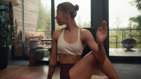 a blonde girl in a white top does yoga and does an exercise to stretch and strengthen the spine on a special carpet in an industrial house overlooking a coniferous forest