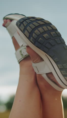 primer plano de piernas en sandalias blancas levantadas contra el brillo cálido de la luz solar, fondo borroso suave presenta árboles en la distancia, creando un entorno al aire libre relajante y pacífico con luz dorada y vibraciones naturales