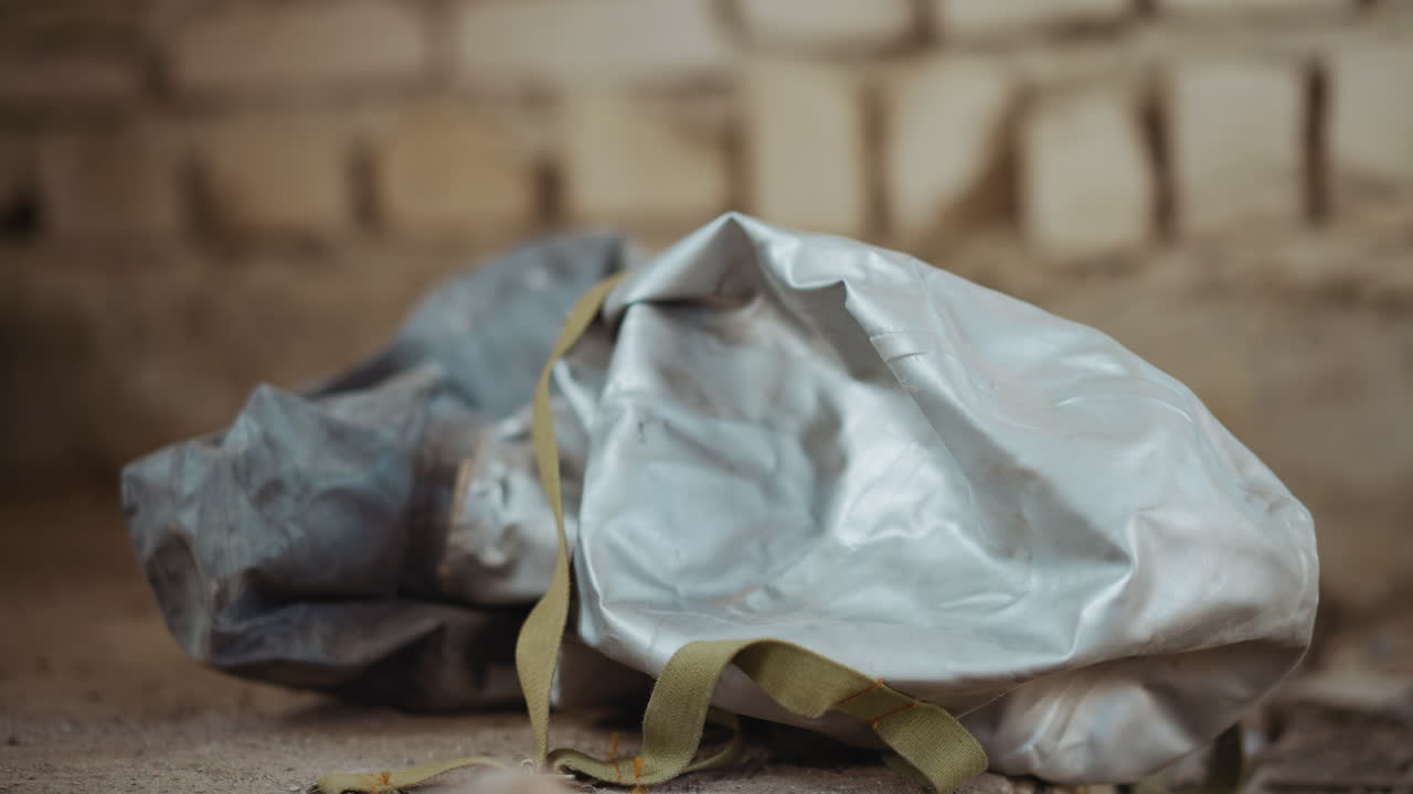 Close up of hazmat mask falling onto cracked dusty floor inside dim industrial setting, with soft light highlighting creases in protective surface and gritty texture of environment