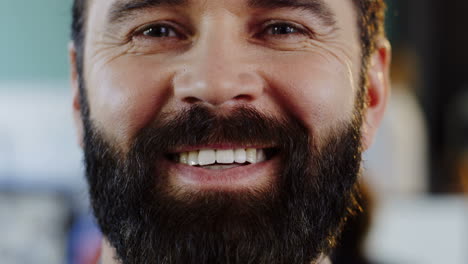 vista cercana del hombre barbudo caucásico sonriendo a la cámara en la oficina