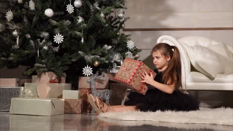 a girl opening christmas presents underneath a christmas tree