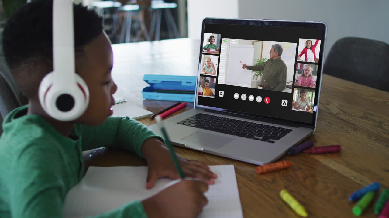 Schoolboy using laptop for online lesson at home, with diverse teacher and class on screen