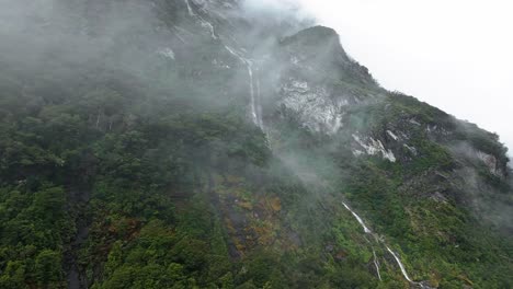 Nebelige-Wolken-Bedecken-Steile-Klippen-Und-Geben-Den-Blick-Auf-Einen-Dünnen-Wasserfall-Frei,-Der-Durch-Den-Wald-In-Neuseeland-Stürzt.